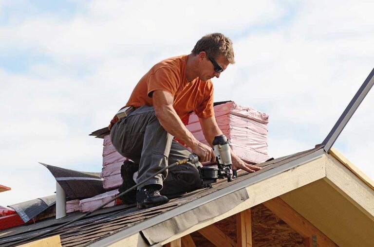 Person placing a bucket beneath a ceiling drip while moving furniture away from the wet area.
