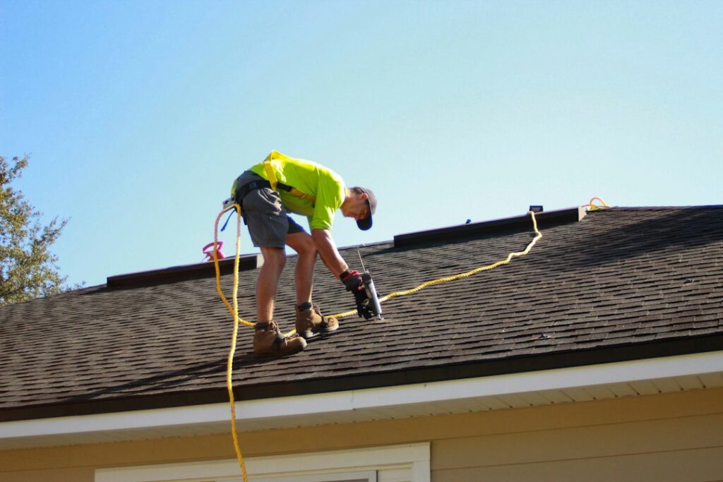 Homeowner reviews a roofing contract and inspection photos at a kitchen table beside a damaged shingle sample.